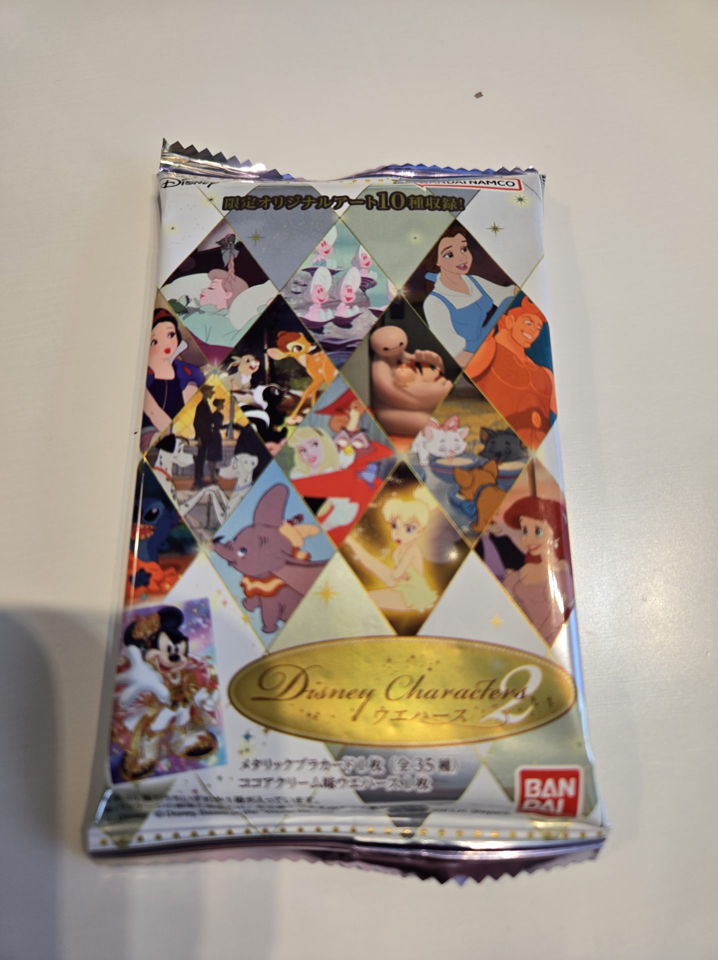 Disney Characters ウエハース2のパッケージ写真。各キャラクターのイラストが菱形パターンに敷き詰められ、バンダイのロゴと「Disney Characters 2」のゴールドのタイトルが入っている