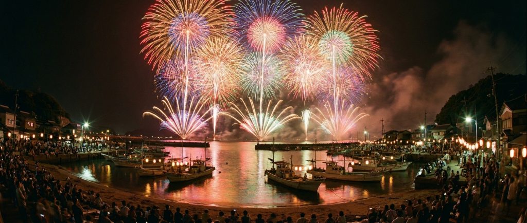 港町の夜空に大輪の花火が上がる夏祭りのイメージ